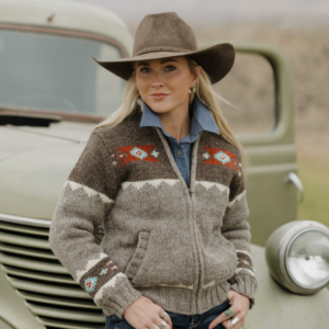 Woman wearing Ladies Navajo Sweater in brown and gray standing by a vintage truck with hands in knit pockets