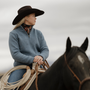 Woman riding horse wearing Ladies Mae wool sweater in chambray blue
